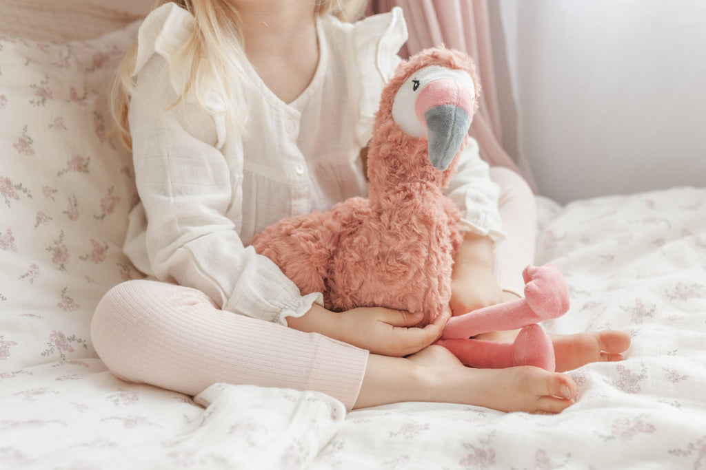 Child holding a pink flamingo plush toy on a soft surface