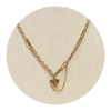 Gold paperclip necklace with a heart pendant on a beige circular stand