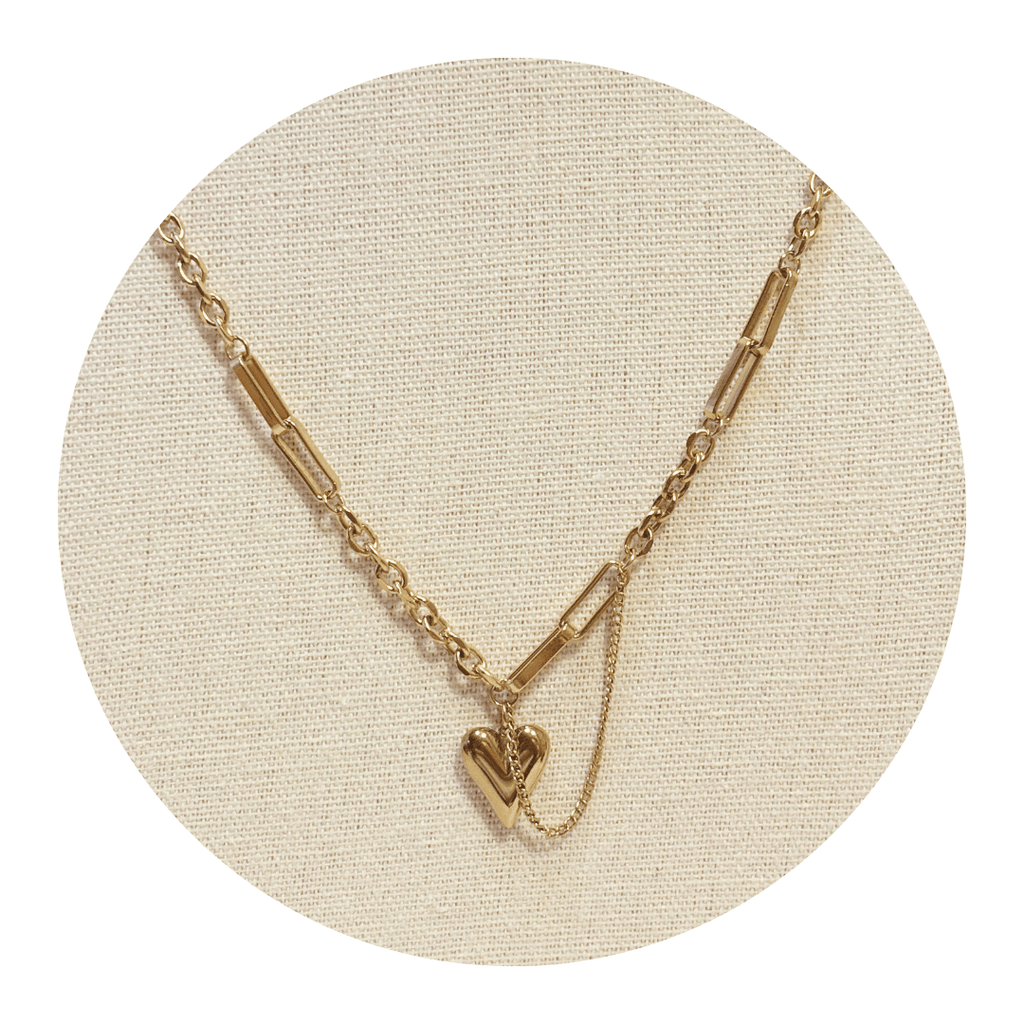 Gold paperclip necklace with a heart pendant on a beige circular stand
