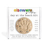 Elseware Unplug 'Day at the Beach Kit' in its white cardboard packaging, featuring a central printed beach paw print made of sand, shells, and stones.