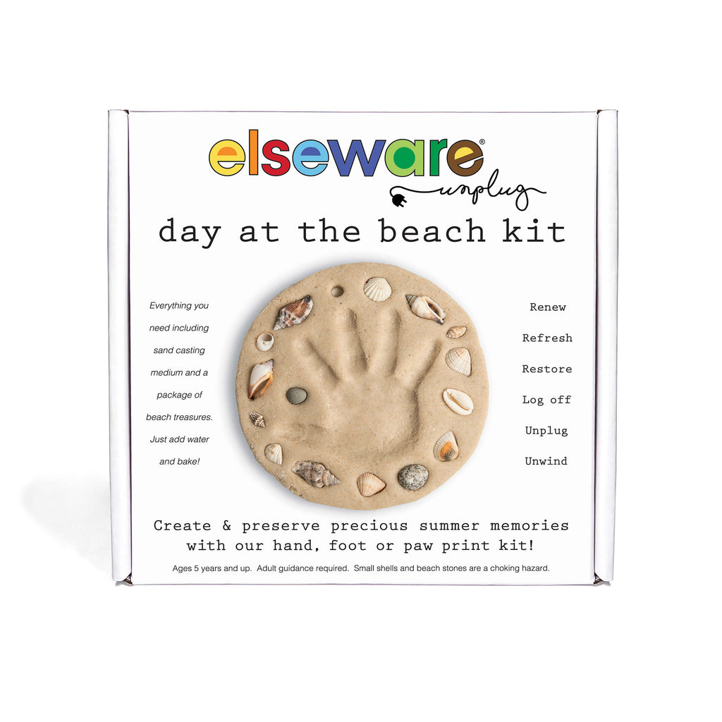 Elseware Unplug 'Day at the Beach Kit' in its white cardboard packaging, featuring a central printed beach paw print made of sand, shells, and stones.