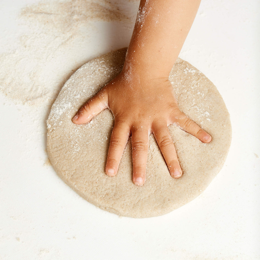 Hand pressing into a round piece of dough on a light background