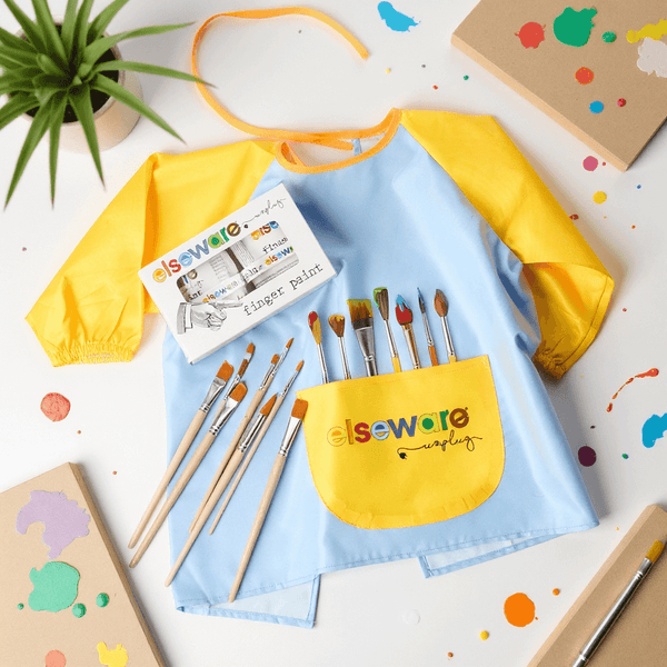 Children's art apron with paintbrushes and paint containers on a white surface with paint splashes.