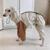 Dog wearing a beige raincoat and brown pants indoors.