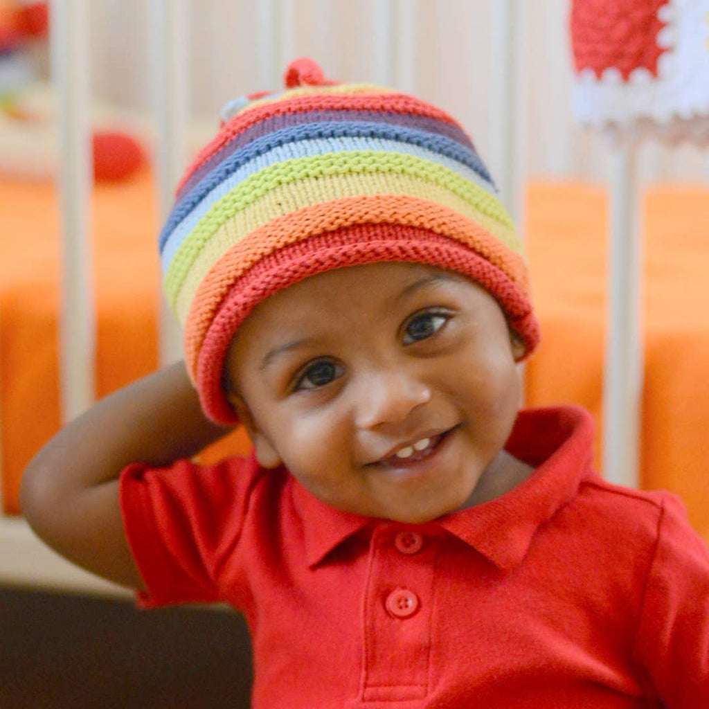 Child wearing a colorful striped hat and red shirt in a crib