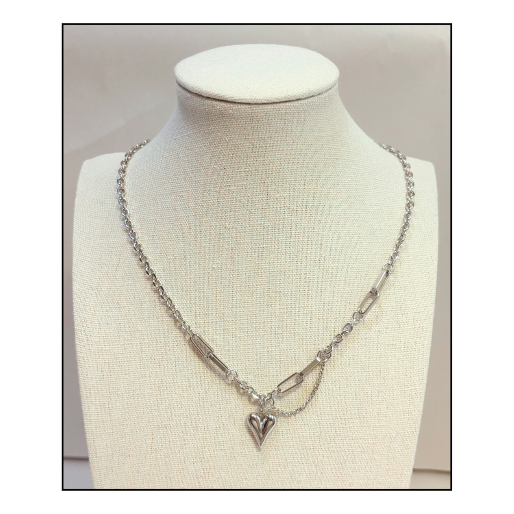 Silver necklace with a heart pendant on a paperclip chain on a mannequin bust.
