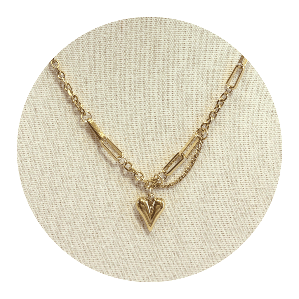 Gold necklace with a heart pendant on a beige circular stand