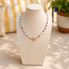 Colorful beaded necklace on a mannequin bust with a striped cushion and plant in the background