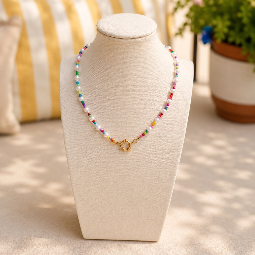Colorful beaded necklace on a mannequin bust with a striped cushion and plant in the background