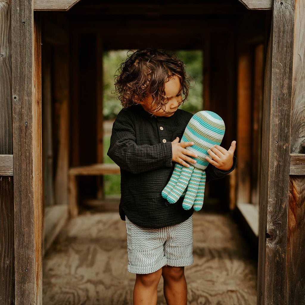 Child holding a striped toy inside a wooden playhouse