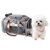 A gray and blue pet carrier bag with brown straps, shown next to a small white fluffy dog wearing a pink collar on a plain white background.