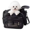A small white fluffy dog sits inside a black pet carrier bag with mesh pockets and side straps, photographed on a plain white background.