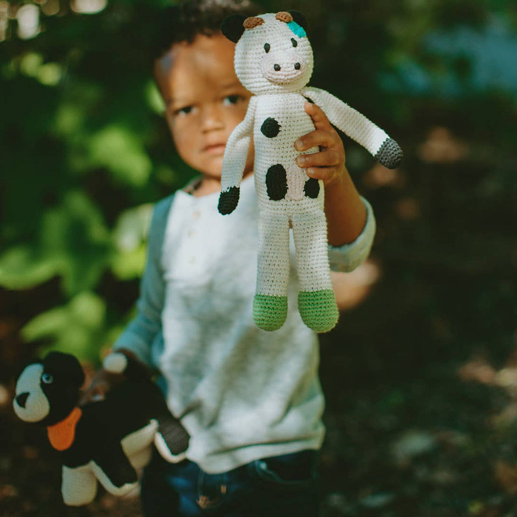 Child holding a crochet cow toy outdoors with greenery in the background