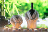 Wine bottles wrapped in bathrobes with candles on a wooden surface, blurred greenery in the background
