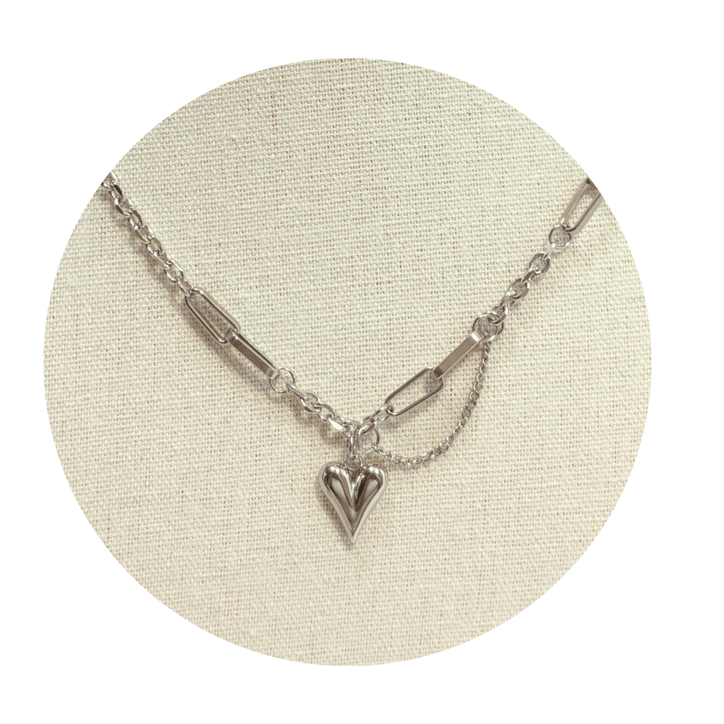 Platinum color necklace with a heart pendant on a beige circular stand