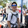 Man carrying a small white dog on his shoulders at an outdoor event.
