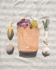 Peach-colored bag with plush vegetable dog toys on a striped fabric background