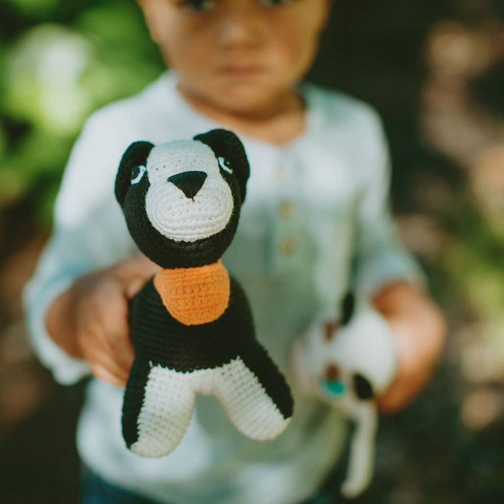 Child holding a small crocheted panda bear toy outdoors.