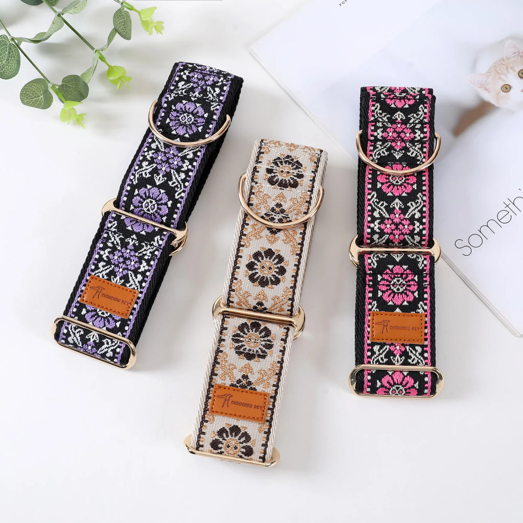 Three woven pet collars with gold-tone hardware are arranged on a white surface. The left collar is black with purple floral patterns, the center collar is cream with black floral patterns, and the right collar is black with pink floral patterns.