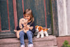 Child sitting on steps with two plush toys in front of a wooden door.