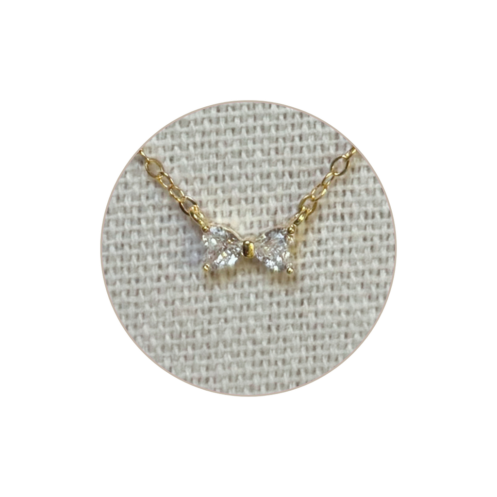Gold necklace with a bow pendant on a gray textured background