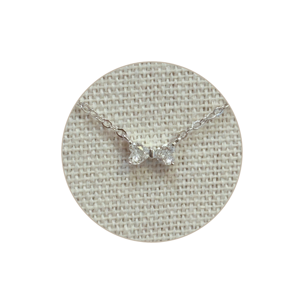 Silver necklace with a diamond bow pendant on a textured gray background