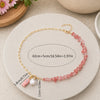 Necklace with pink beads and a pearl charm on a round stone surface with measurements.