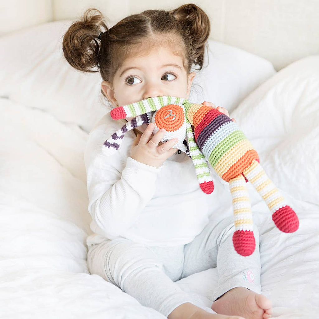 Child holding a colorful striped toy on a white couch