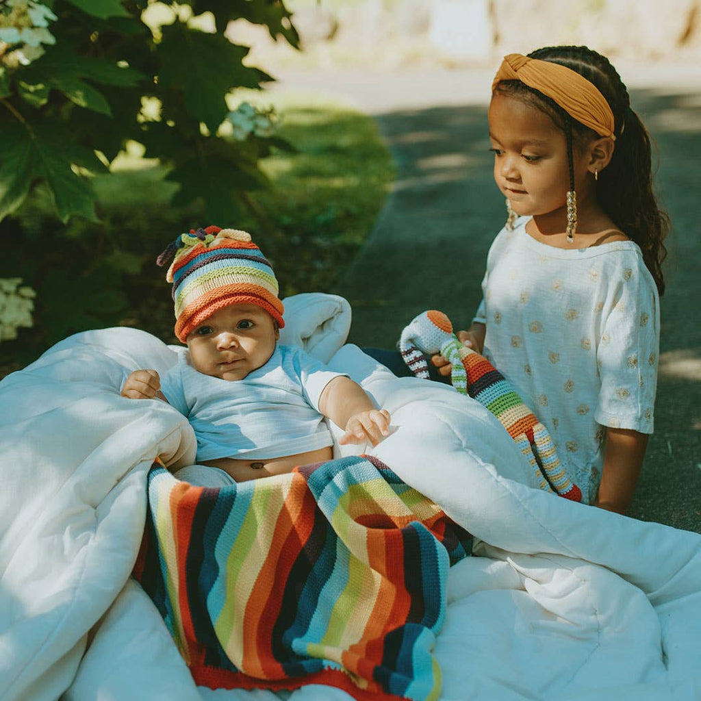 Two children sitting on a blanket outdoors with colorful items.