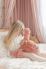 Child holding a pink flamingo plush toy in a bedroom with pink curtains.